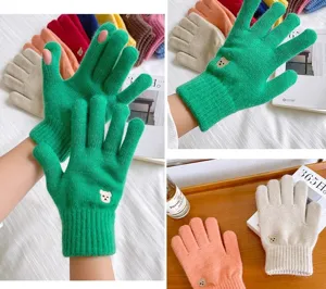 Primer plano de lindos guantes de invierno de punto con bordado de osito y dedos táctiles.