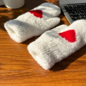 Close up detail of white plush winter mittens featuring a red heart pattern on wooden table.
