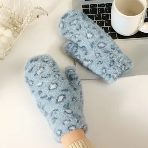 Close-up of cozy blue fluffy leopard mittens on a white desk with laptop and cup.