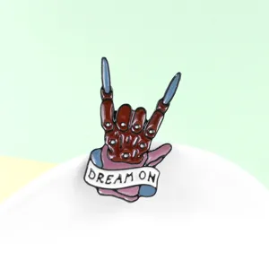 Punk style metal enamel brooch featuring a skeleton rock gesture hand with DREAM ON banner.