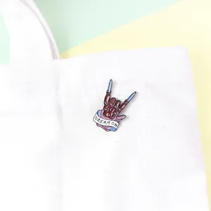 Detailed close-up of a punk-style skeleton hand enamel pin featuring Dream On text.