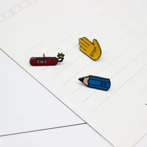 Close-up detail shot of cute cartoon enamel pins featuring pencil, dynamite, and stop gesture design.