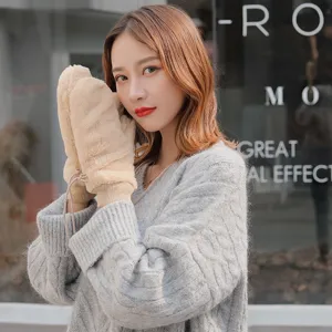 Close-up of fluffy plush winter mittens in beige with cozy knit sweater, soft warm fabric.