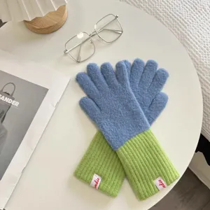 Detailed view of fashionable colorblocked knit gloves displayed on white table, cozy winter style.