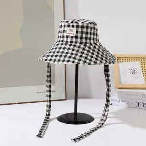 Vue détaillée du chapeau bob à carreaux noir et blanc avec de longs liens et écusson.