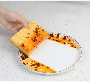 Detail shot of kitchen cleaning sponge wiping oil off ceramic plate, showing strong absorption.