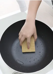 Close-up detail shot of sisal wood pulp sponge cleaning black frying pan in kitchen sink.
