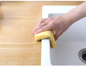 Close-up detail shot of a kitchen cleaning sponge cleaning the sink edge in a modern home kitchen.