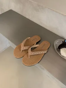 Gedetailleerd overzicht van beige geweven teenslipper met metalen studs chique zomermode.