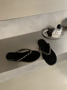 Detailopname van stijlvolle zwarte teenslippers met gouden klinknagels op de bandjes.