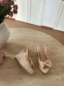 Dettaglio in primo piano di sandali con zeppa beige e plateau con fiocco e suola in corda.