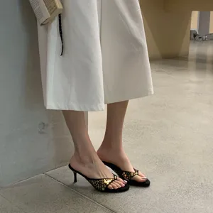 Vista de cerca de sandalias de dedo para mujer en ante negro con tachuelas doradas y tacones finos.