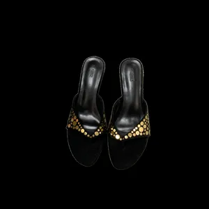 Detalle de sandalias de tacón de aguja en ante negro con tachuelas doradas brillantes.
