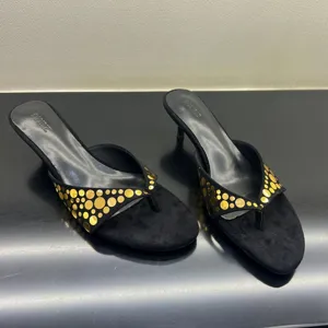 Primer plano de sandalias de tacón bajo en ante negro con elegantes remaches dorados.