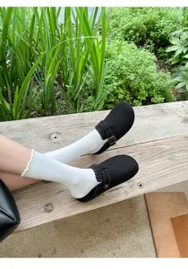 Detailansicht schwarzer kuscheliger Fell-Clogs kombiniert mit weißen Socken im Freien.