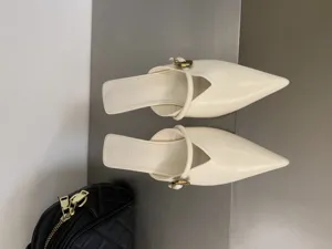 Primo piano di sabot a punta bianco crema con cinturino delicato e tacco kitten.