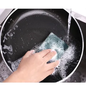 Close-up detail shot showing wood pulp sponge cleaning a frying pan in kitchen sink.
