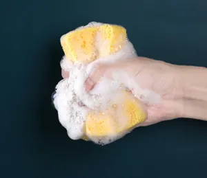 Nahaufnahme des gelben Holzzellulose-Schwamms mit reichlich Schaum für die Küchenreinigung.