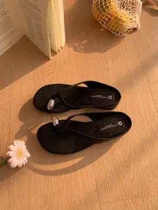 Detail shot of minimalist black thong sandals with metal accent for women summer beach.