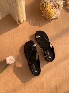 Detailed view of black minimal thong sandals with metallic accent in a cozy lifestyle setting.