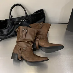 Vue détaillée de bottes western marron à bout pointu avec boucles élégantes et brides cloutées.