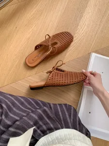 Mules planos trenzados en marrón con punta cuadrada, lazo delicado y diseño de malla calada elegante.