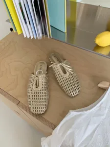 Detalle de mules doradas trenzadas con punta cuadrada francesa, malla calada y tira de cordones.