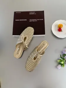 Primer plano de mules planas de malla tejida dorada con lazo, estilo elegante sobre mesa.