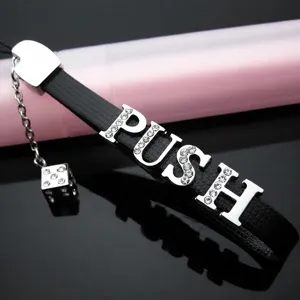 Gros plan détail du bracelet en cuir noir avec lettres PUSH en strass et pendentif dé.