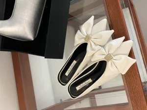 Witte elegante muiltjes met spitse neus, strik en metalen gesp, mooie schoen detail.