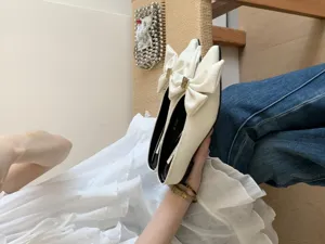 Witte muiltjes met puntneus, grote strik en metalen gesp, elegante platte damesschoenen.