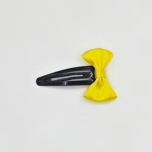 Detail shot of a bright yellow ribbon bow attached to a classic black metal snap hair clip.