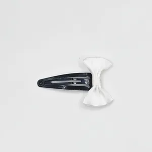 Close up detail of a cute black metal BB hair clip decorated with a clean white bow ribbon.