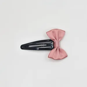 Close-up detail of cute pink satin bow hairpin, simple everyday sweet hair clip accessory.