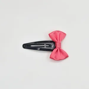 Close-up detail of black metal snap hair clip decorated with pink satin bow hair accessory detail.