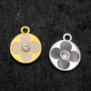 Détail en gros plan de pendentifs trèfle en métal avec strass au centre, dorés et argentés.