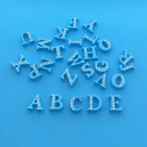 Vue détaillée de pendentifs de lettres peints en bleu et ornés de strass brillants.