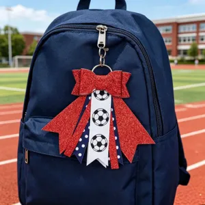 Close-up detail of the red glitter bow soccer keychain hanging on a blue backpack, sports style.