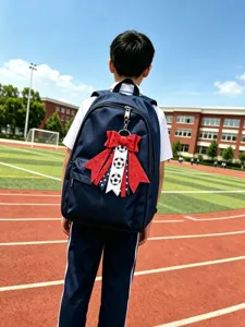 Outdoor detail shot of a navy blue school backpack featuring a red glitter bow and soccer pendant.