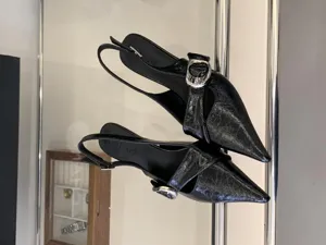 Elegant black slingback pointed-toe heels for women with chic metallic buckle detail.