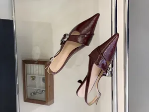 Burgundy patent leather slingback kitten heels featuring sharp pointed toe and metal buckle.