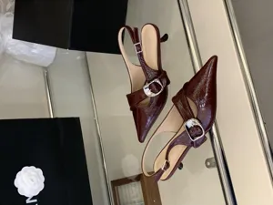 Burgundy patent leather pointed toe slingback kitten heels with striking silver buckle detail.