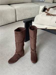 Vista detallada de botas altas marrones de ante para mujer con pliegues suaves y hebilla.