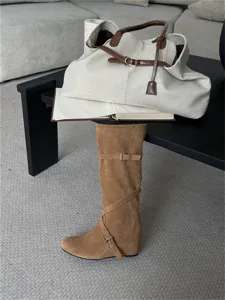 Vista detallada de botas altas de ante marrón con tiras decorativas y tacto suave.