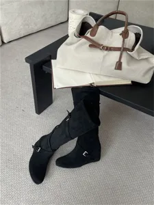 Vista detallada de botas altas de ante negro con punta redonda y correas con hebilla.