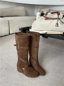 Vista detallada de botas retro de ante marrón con correas de hebilla y pliegues suaves.