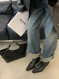 Detailed view of women's black pointed toe chunky heel ankle boots styled with cuffed denim jeans.