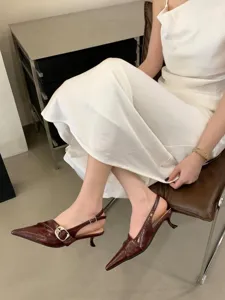Detailed view of dark red pointed-toe slingback kitten heels with metal buckle on model.