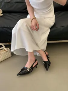 Detailed view of black pointed-toe slingback kitten heels paired with a white dress.