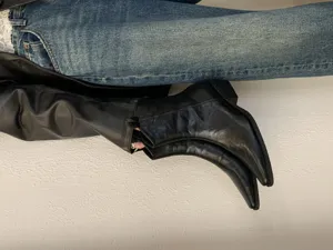 Detailed shot of women's black pointed-toe chunky heel boots styled with denim jeans.
